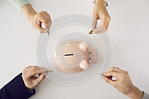 From above shot of people& x27;s hands putting money in pink piggy bank on white background