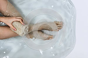 Above shot of woman`s legs and hands holding luffa sponge in bathtub