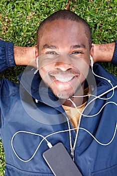 Above of smiling young black man lying on grass listening to music with earphones