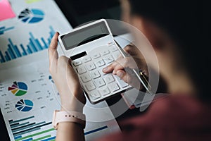 Above view of accouting woman consultant holding pen and using calculator with financial report on wooden desk at home