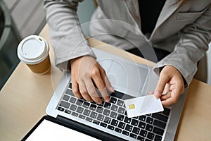 Above view of businesswoman holding credit card making purchase or paying online on laptop.