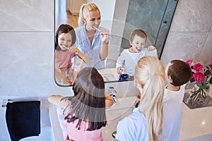 Above view of caucasian family using toothbrushes and looking in mirror. Young caucasian mother in pyjamas standing with