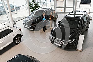 Above view of cheery millennial couple speaking to car salesman about purchasing or renting new vehicle at dealership