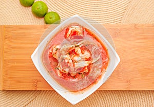 Above view of delicious traditional ecuadorian shrimp cebiche in rectangular white bowl, with lemon, served over a photo