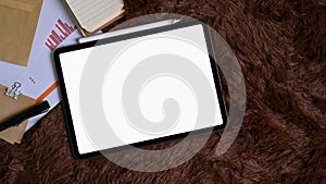 Top view of digital tablet, document and notebook on brown fur rug.