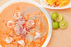 Above view of Ecuadorian food: shrimp cebiche with some chifles inside white bowl, lemon in a wooden table background photo