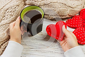 Above view of female hand holding hot cup of coffee with red heart on wood table. Photo in vintage color image style