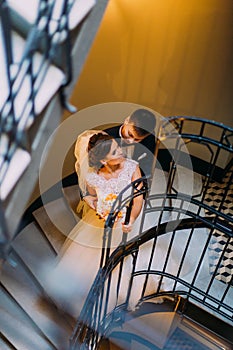 The above view of the groom hugging the bride back while standing on the stairs.