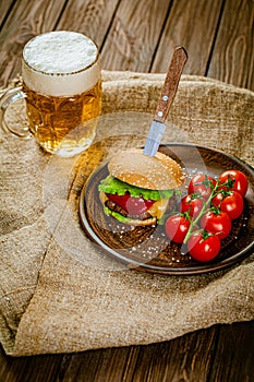 From above view of homemade burger on rustic wooden serving table with pint of beer. Selective focus