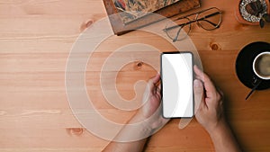 Above view man hands holding smart phone with empty screen on wooden desk.