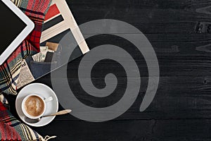 Above view of newspaper, scarf in a cage, tablet and cup of latte coffee on black wooden background.