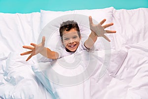 Above view portrait of excited cheerful small boy lay cozy sheets cushion blanket raise arms you isolated on turquoise