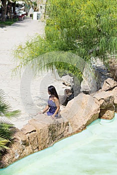 Above view of a pretty young hispanic woman sitting on rock next to a water pond