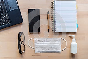 Above view of remote work kit on wooden office desk with hand sanitizer and face mask, a solution against the spread of corona photo