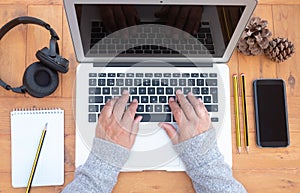 Above view of senior woman`s hands working on laptop. Wooden table. Alternative outdoor office. Cellphone and headphones close to