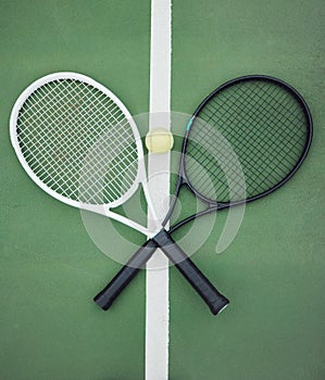 Above view of two tennis rackets and a ball on an empty court in a sports club. Aerial view of black and white tennis