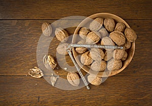 Above View of Walnuts grown in Oregon, in a Wooden Bowl on a Dark wood Table Background with some cracked and the nutcracker.