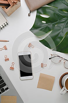 Above view of white office desk with phone, glasses, coffee cup and stationery.