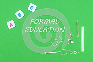 From above wooden minitures school supplies and ABC letters on green background with text formal education