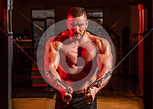 Abs and biceps. Fitness man execute exercise with exercise-machine Cable Crossover in gym. Handsome man with big muscles