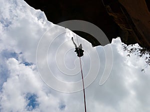 Abseiling a negative sanstone rock wall with blue sky on background - view from bellow