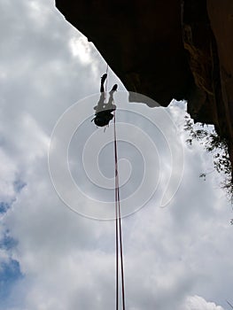 Abseiling a negative sanstone rock wall with blue sky on background - view from bellow