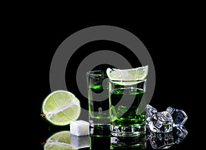 Absinthe shots with lime slices and sugar on black background