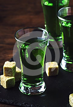 Absinthe - strong alcoholic drink, green bitter wormwood tincture in glasses on the old wooden table, place for text