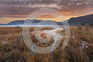 Absolutely stunning vibrant Autumn sunrise landscape image looking from Manesty Park in Lake Distict towards sunlit Skiddaw Range