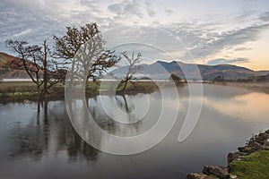 Absolutely stunning vibrant Autumn sunrise landscape image looking from Manesty Park in Lake Distict towards sunlit Skiddaw Range