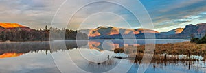 Absolutely stunning vibrant Autumn sunrise landscape image looking from Manesty Park in Lake Distict towards sunlit Skiddaw Range