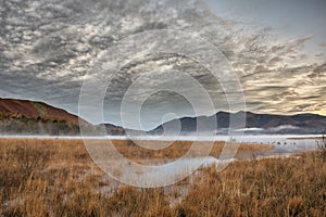 Absolutely stunning vibrant Autumn sunrise landscape image looking from Manesty Park in Lake Distict towards sunlit Skiddaw Range