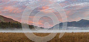 Absolutely stunning vibrant Autumn sunrise landscape image looking from Manesty Park in Lake Distict towards sunlit Skiddaw Range