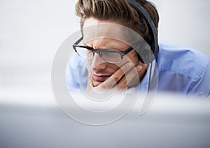 Absorbed in his work. A handsome young businessman wearing a headset while concentrating on his computer screen.