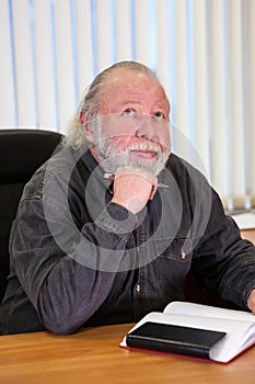 Absorbed pensive mature businessman thinking about problem with pan in hand and notebook on the table