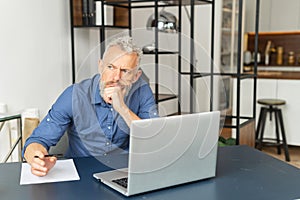 Absorbed pensive senior businessman in smart casual shirt sits at the desk