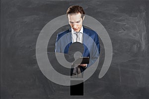 Abstract attractive businessman with tablet and question mark shape on chalkboard wall background. FAQ and answer concept