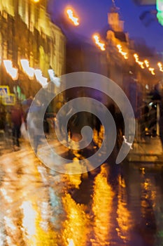 Abstract background of blurred people figures under umbrellas, city street in rainy evening, orange-brown tones