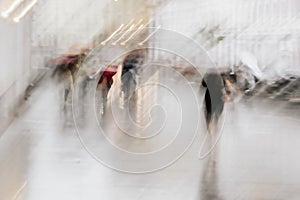 Abstract background of blurred people under umbrellas, city street in rain, impressionism style. Intentional motion blur