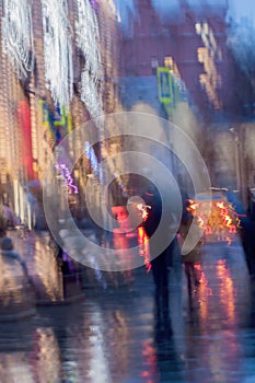 Abstract background of blurred Woman with girl under umbrella, city street in rainy. Intentional motion blur