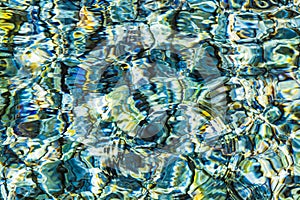 Abstract background of clear sea or river water ripple waves in blue, green, yellow color. Sea water with different color pebbles