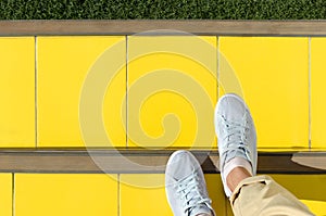 Abstract background - foots in light blue sneakers are on stairs covered with yellow tiles, ahead green lawn.