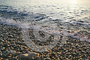 Abstract background of oncoming sea wave surf on pebble beach closeup on sunrise