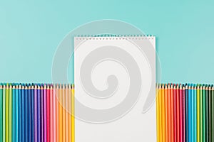 Abstract background for painting, drawing and sketching. Blank white paper spiral notebook and many colored pencils on