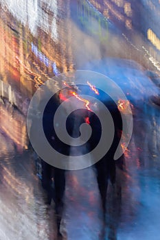 Abstract background of people hurrying down the city street in rainy evening, shop windows. Intentional motion blur