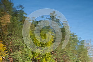 Abstract background: reflection of autumn deciduous forest in the pond. Blue sky and leaves reflecting in a lake. Water