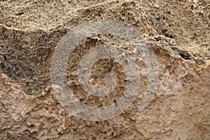 Abstract background of sandy rocks with holes close-up. Brown background of wrinkled uneven sand texture