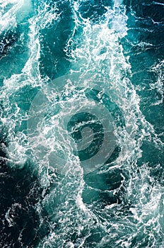 Abstract background. The waves of the sea water meet with underwater pointed rocks, forming whirlpools.