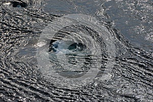 Abstract background. The waves of the sea water meet with underwater pointed rocks, forming whirlpools.