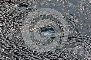 Abstract background. The waves of the sea water meet with underwater pointed rocks, forming whirlpools.